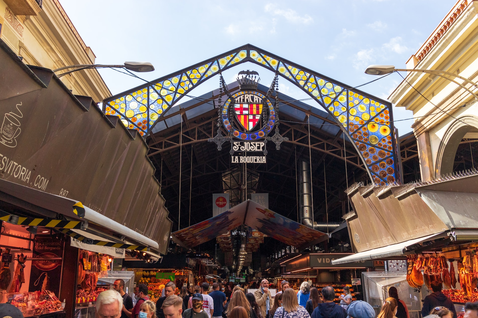 people walking towards st-josep la boqueria entrance, market stalls on either side.